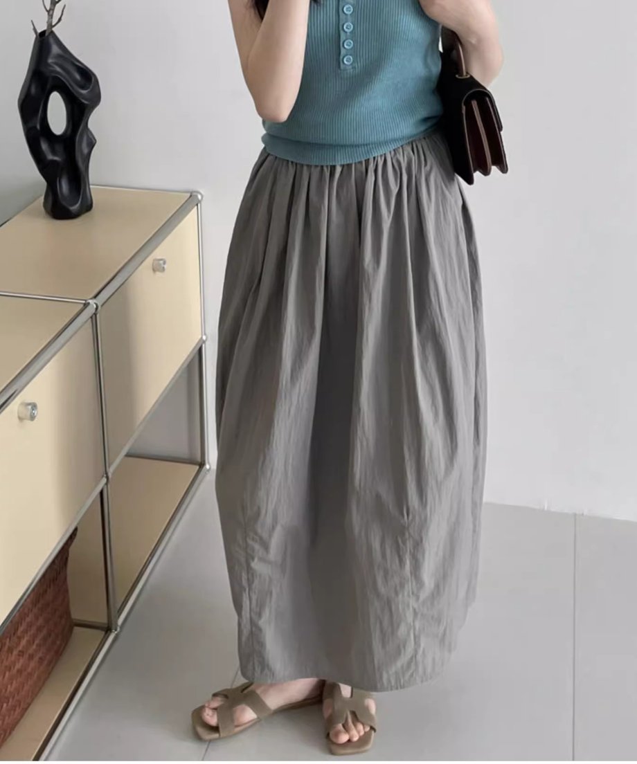 ターコイズブルーのタンクトップとグレーのロングバドスカートを着用し、バッグを持った女性の姿。スカートのドレープ感がわかる。
