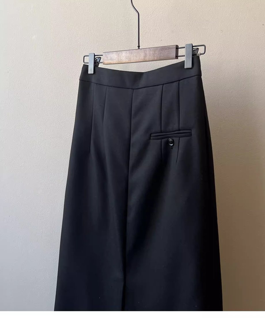 黒のストレートロングタックスカートをハンガーにかけた後ろ姿。片玉縁ポケットとセンターバックのタックが見える。