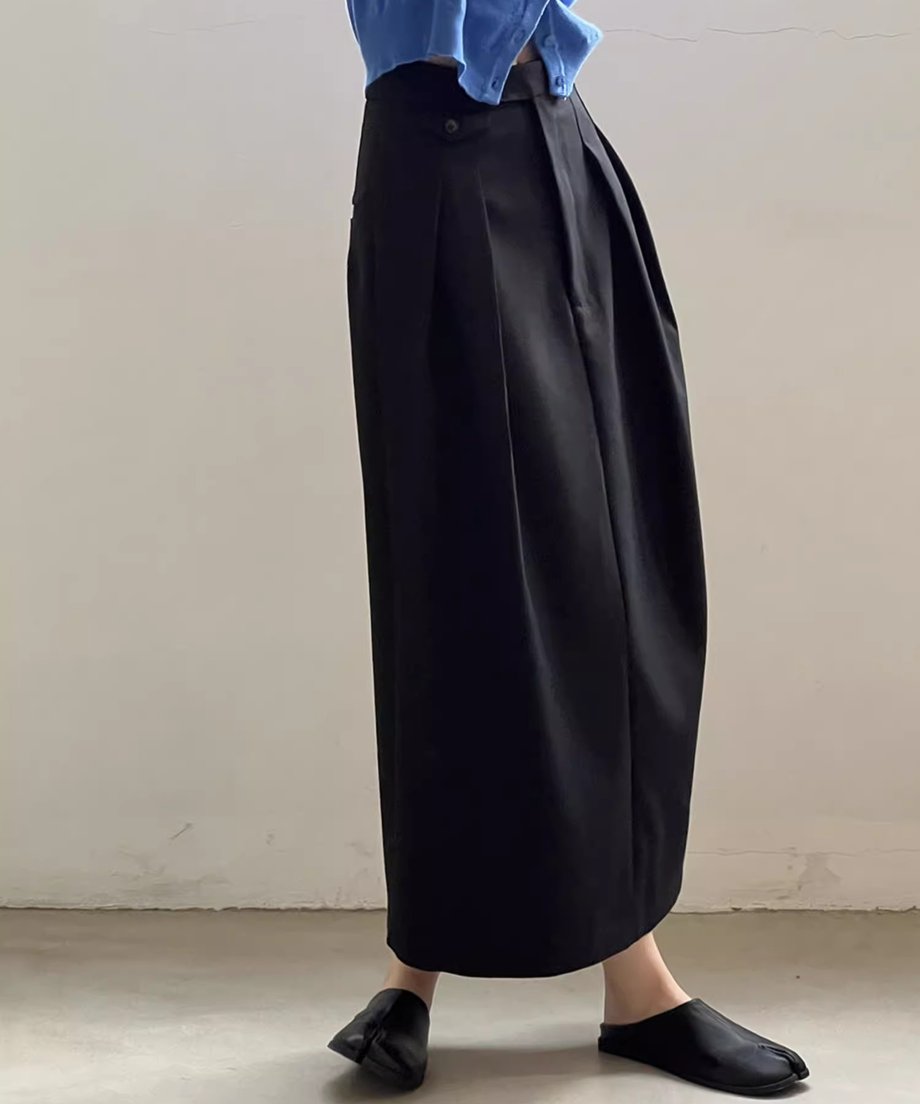 黒のストレートロングタックスカートを着用し、青いトップスを着用した女性が室内で立っているショット。