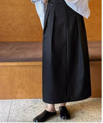 黒のタックスカートにストライプのシャツをコーディネートしたスタイル。カフェのような木製の内装を背景に立っている。