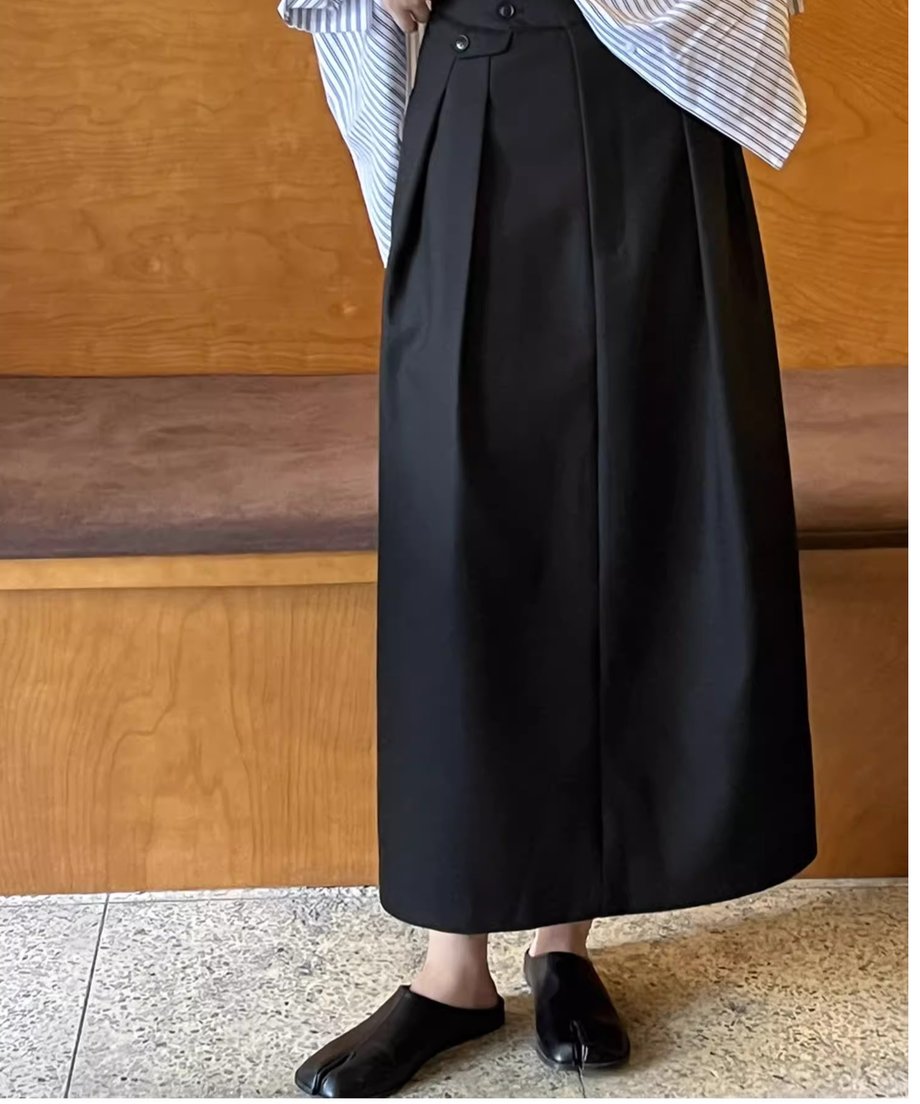 黒のタックスカートにストライプのシャツをコーディネートしたスタイル。カフェのような木製の内装を背景に立っている。