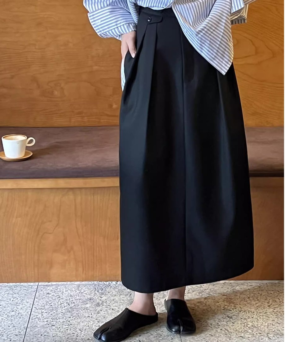 黒のタックスカートにストライプのシャツをインしたスタイル。カフェのような木製の内装を背景に立っている。