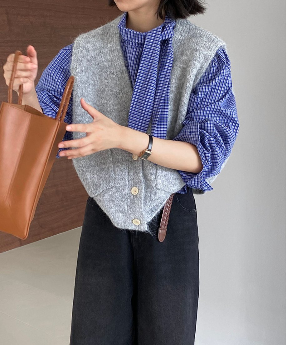 グレーのウールブレンドニットベストを青いチェック柄のシャツと黒いワイドパンツに重ね着している女性のショット。
