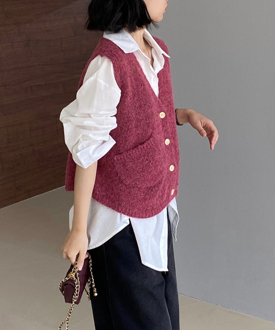ワインレッド色のVネックニットベストを白い長袖シャツと黒いボトムスに重ねて着用している女性のサイドからのショット。