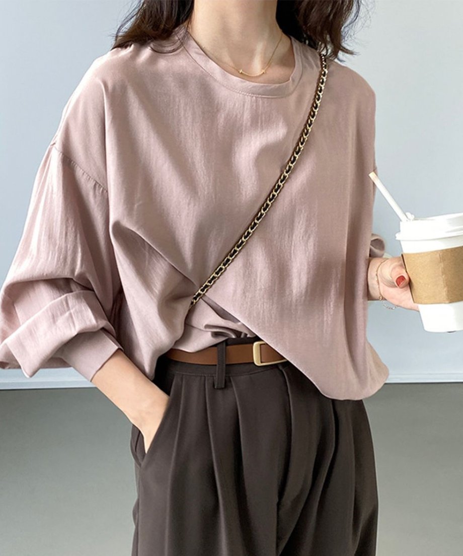ダークブラウンのプリーツ入りワイドレッグスーツパンツにピンクベージュのオーバーサイズTシャツをタックインし、茶色の細ベルトを締めた女性のクロップドショット