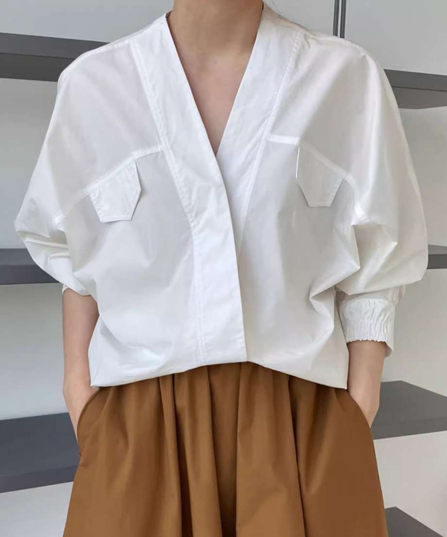 Vネックとドルマンスリーブの白いシャツを、茶色のワイドスカートにインして着用している女性のウエストアップショット