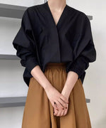 Vネックとドルマンスリーブの黒いシャツを、茶色のフレアスカートにインして着用している女性のウエストアップショット