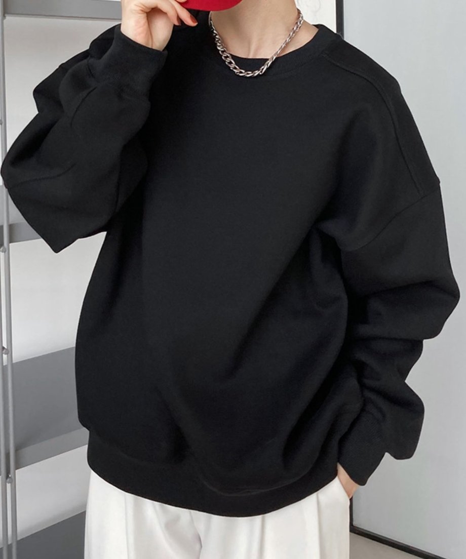 黒のオーバーサイズスウェットシャツを着用し、白のワイドパンツを合わせた女性の半身像。
