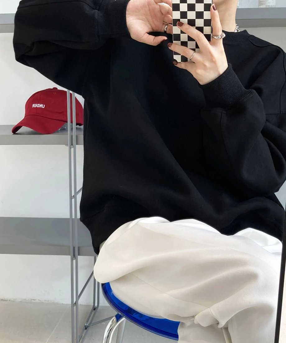 黒のオーバーサイズスウェットシャツを着用し、白のワイドパンツを合わせた女性が椅子に座っているショット。