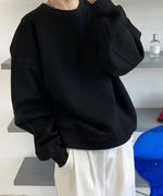 黒のオーバーサイズスウェットシャツを着用し、白のワイドパンツを合わせた女性の半身像。