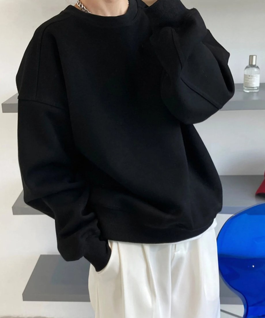 黒のオーバーサイズスウェットシャツを着用し、白のワイドパンツを合わせた女性の半身像。