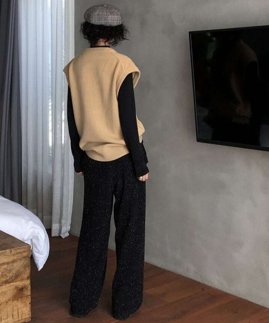 ベージュのニットベストと黒の長袖インナーに、黒のネップ入りニットワイドパンツを合わせた後ろ姿。チェック柄のキャップを着用し、屋内（寝室）で撮影。