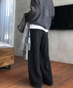 黒のネップ入りニットワイドパンツを着用し、横向きで全身を写した画像。トップスはグレーのニットと白のインナーをレイヤード。手にはマフラーを持っている。