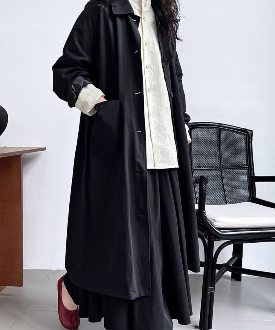 オフホワイトのシャツに黒のロングコートと黒のロングスカートを合わせた、モノトーンのレイヤードスタイル。足元には赤いシューズ。
