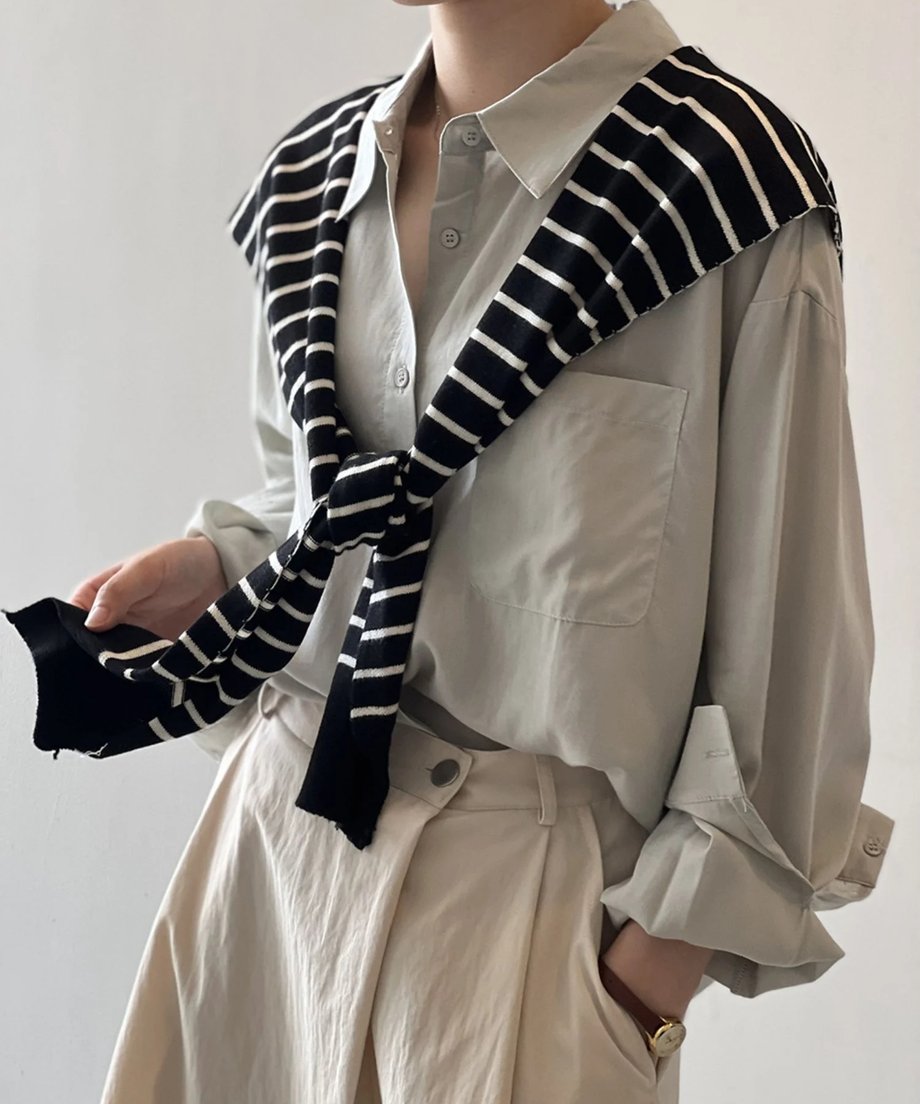 ライトベージュのロングシャツワンピースに、白と黒のストライプ柄ニットスカーフを肩にかけた女性の全身画像。