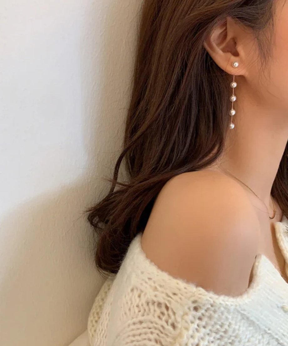 白いニットを着用した女性の耳元に、チェーンで4粒のパールが連なったロングピアスが揺れている様子。