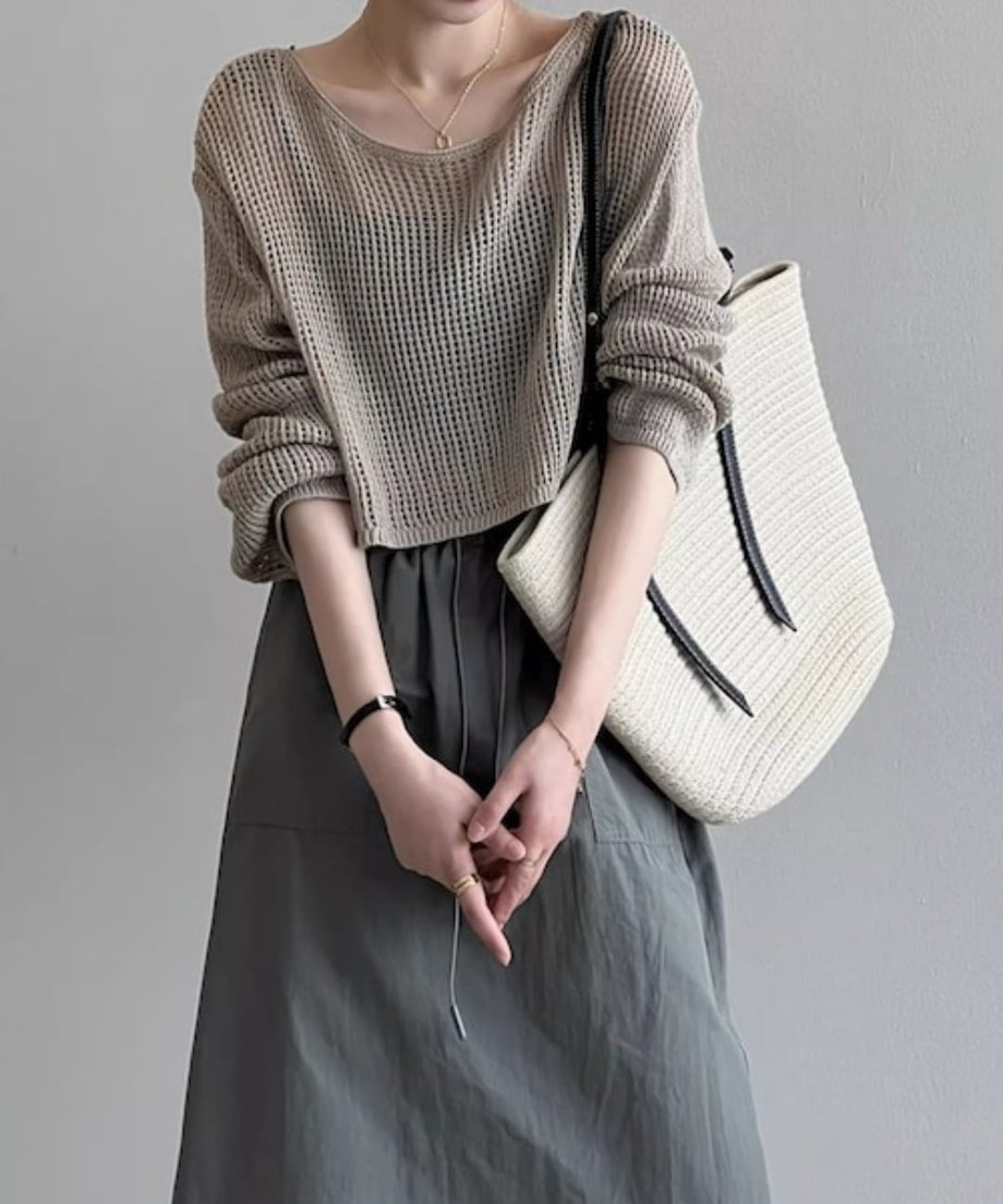 ミルクティー色のメッシュニットにカーキのドローストリングスカートを合わせ、白いバッグを肩にかけた女性。