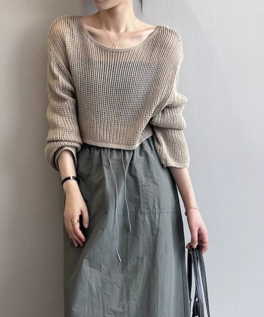 ミルクティー色のメッシュ編みクロップド丈セーターとカーキのロングスカートを着用した女性。