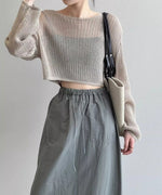 ミルクティー色のメッシュニットにカーキのドローストリングスカートを合わせ、バッグを肩からかけた女性。