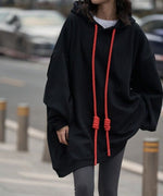 黒のオーバーサイズロングパーカーを着用した女性が、ポケットに手を入れながら立っている上半身のクローズアップ。