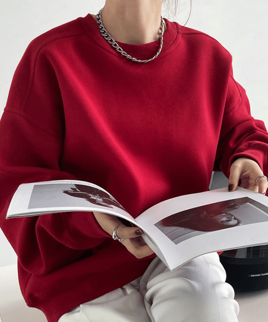 レッドのオーバーサイズスウェットを着用し、雑誌を読む女性のクローズアップ。
