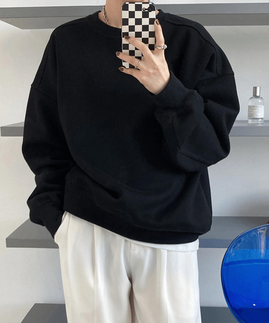 ブラックのオーバーサイズスウェットと白のワイドパンツを合わせ、片手をポケットに入れた女性のクローズアップ