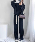 ブラックのVネックショートスウェットと黒のパンツを合わせた女性の全身ショット。ブラウンのバッグとスマホを手に持っている。