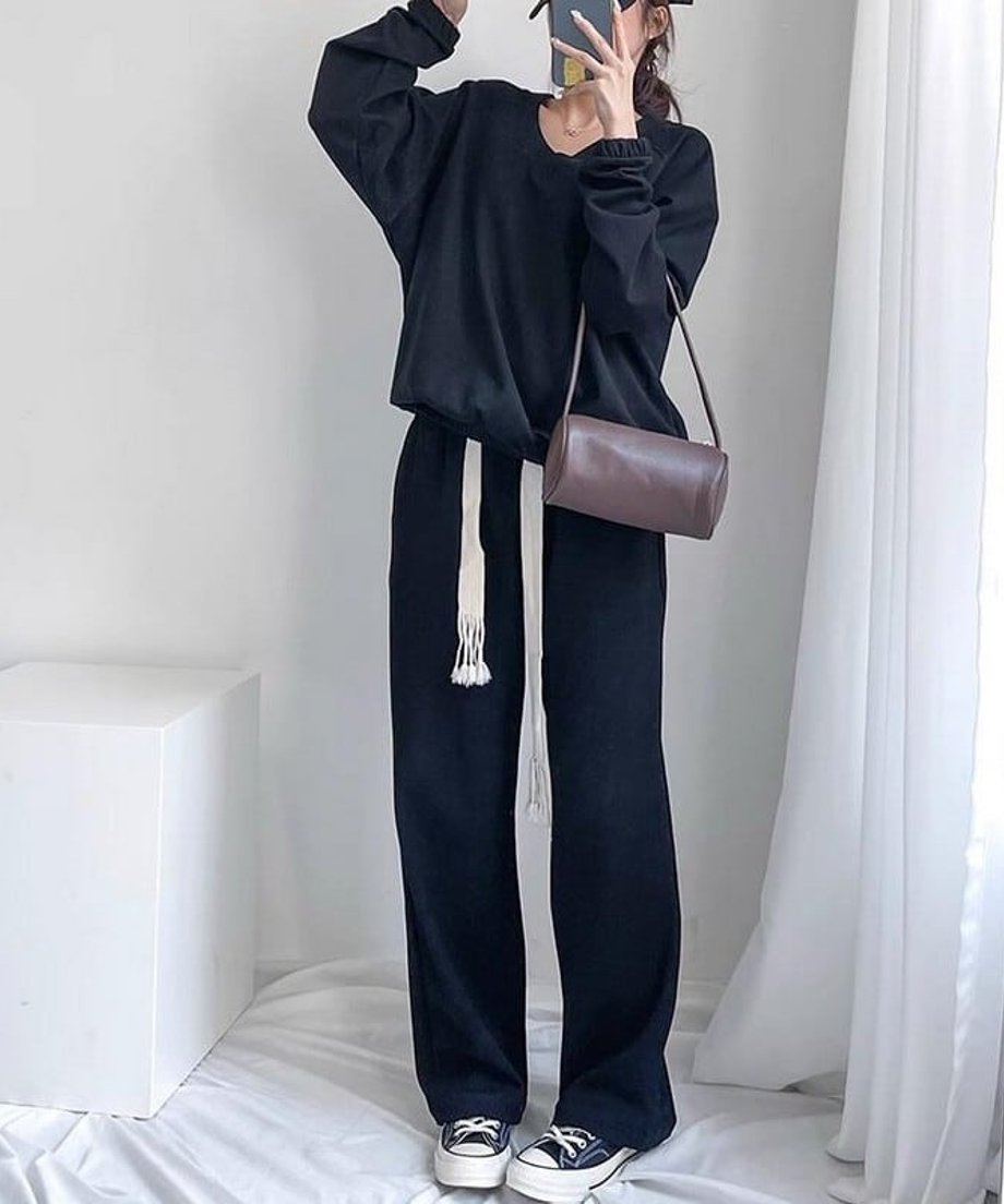 ブラックのVネックショートスウェットと黒のパンツを合わせた女性の全身ショット。ブラウンのバッグとスマホを手に持っている。