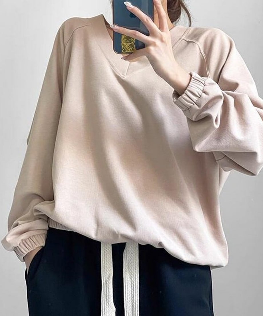 アプリコットのVネックショートスウェットを黒のパンツに合わせた女性のクローズアップ。