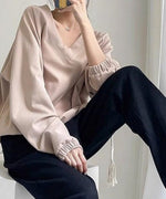 アプリコットのVネックショートスウェットを着用し、黒のスウェットパンツを合わせた女性が座っているショット。
