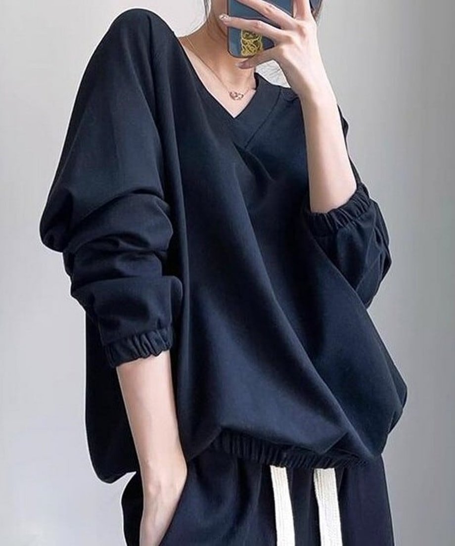 ブラックのVネックショートスウェットと黒のパンツを合わせ、ポケットに手を入れた女性のバストアップ。