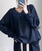 ブラックのVネックショートスウェットと黒のパンツを合わせた女性のバストアップ。スマホを手に持っている。