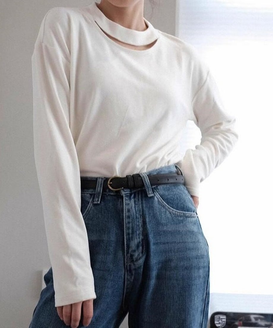 オフホワイトの長袖スリットネックトップスを濃いデニムパンツに黒の細ベルトを合わせて着用した、ウエストアップのファッション画像。