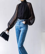 黒のドット柄シアーブラウスをハイウエストデニムにタックインし、手をポケットに入れたポーズ。