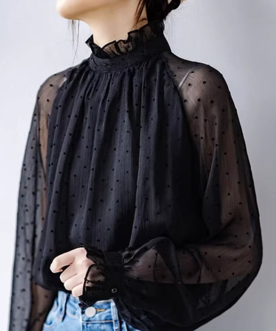 黒のドットシアーブラウスを着用した女性の胸元から肩にかけてのクローズアップ。透け感が際立つ。