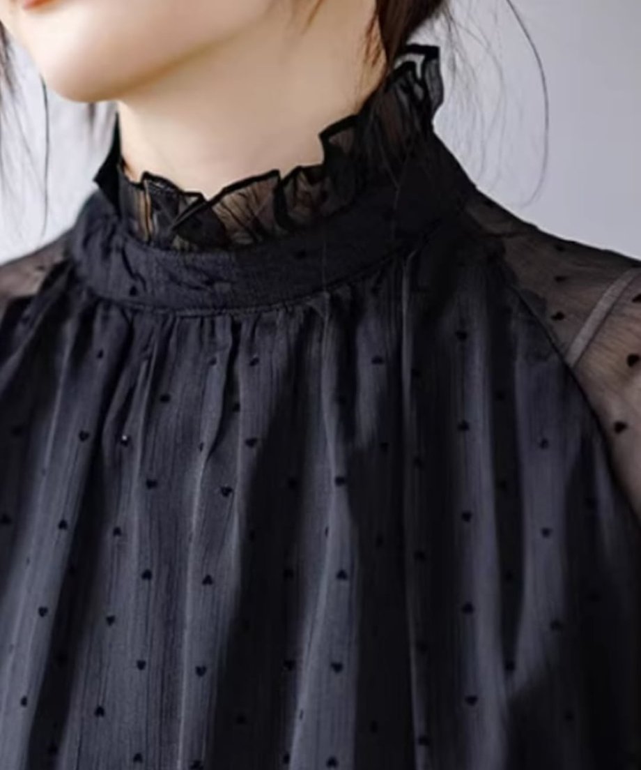 黒のドット柄シアーブラウスを着用した女性のバストアップ。首元はフリルネックのデザイン。