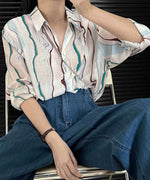 マーブル柄シアーシャツをデニムのワイドパンツと合わせ、椅子に座っている女性の全身像。