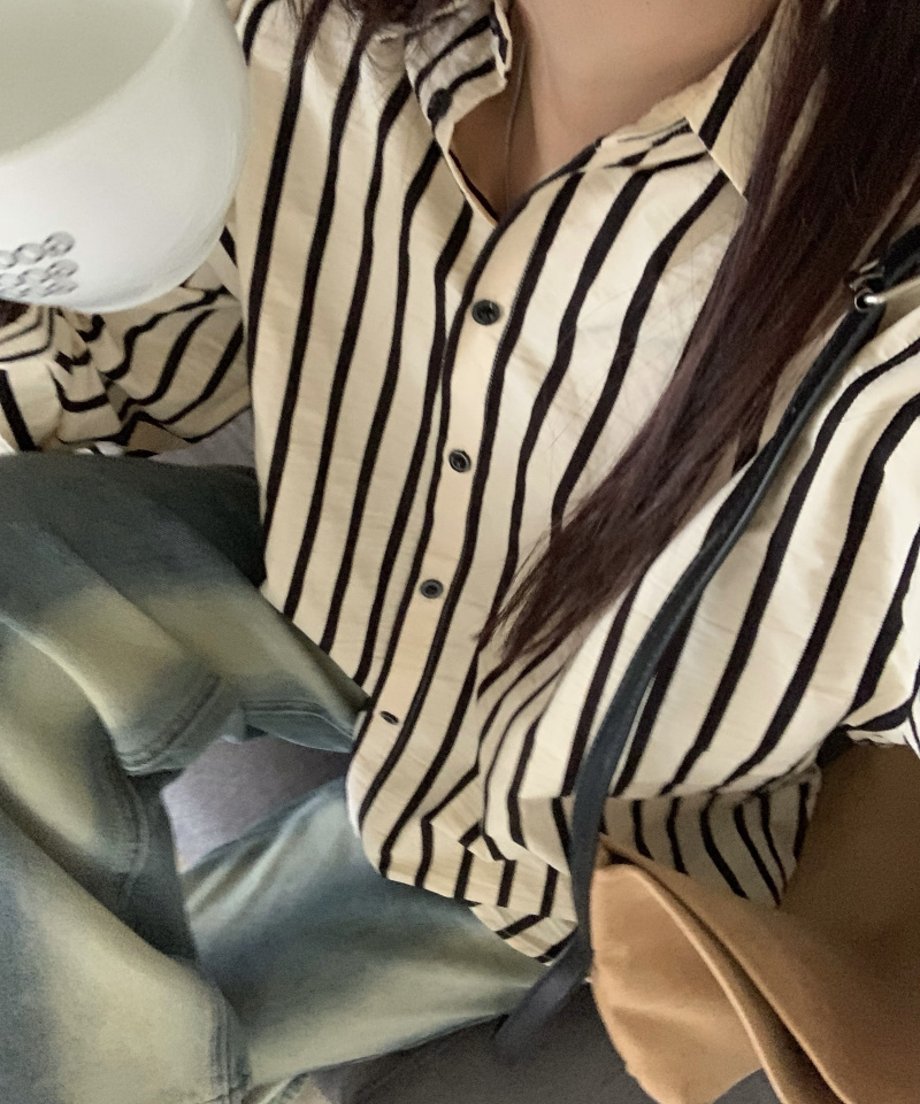 ストライプシャツとウォッシュ加工のデニムを着用し、飲み物を持っている女性のクローズアップ。