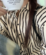 オフホワイトに黒のストライプが入った長袖シャツを着た女性のクローズアップ。コーヒーカップを持ち、デニムを着用。