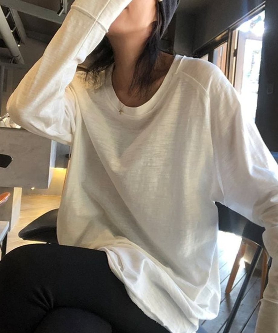 ホワイトのロングスリーブTシャツに黒のスキニーパンツを合わせ、屋外のウッドデッキで座っている女性。