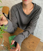 グレーのロングスリーブTシャツを着用した女性のバストアップ。ネックレスを着用し、柔らかな生地感が確認できる。