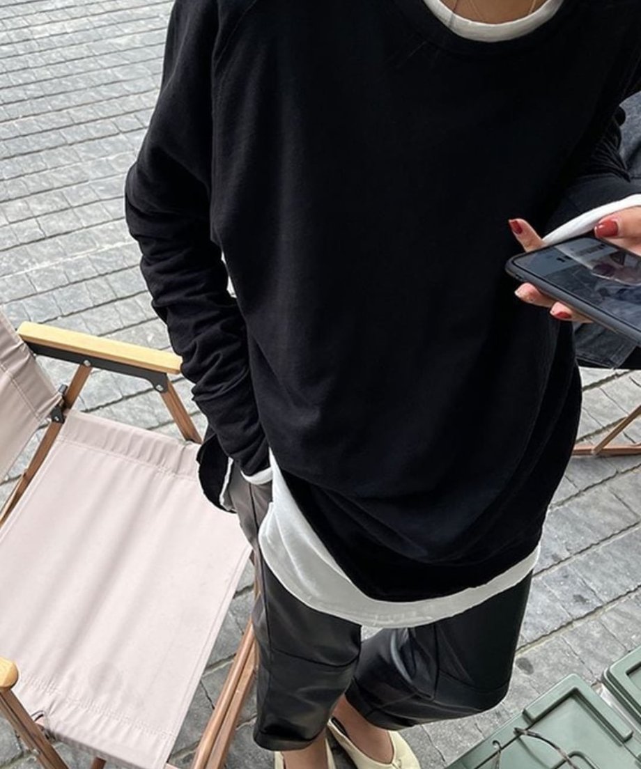 ブラックのロングスリーブTシャツに黒のレザー調パンツを合わせ、白のインナーを裾から覗かせた女性の全身ショット。