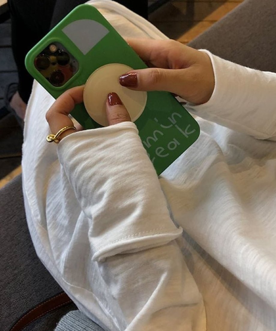 ホワイトのロングスリーブTシャツを着用した女性が手にスマホを持ったショット。袖部分のデザインのクローズアップ画像。