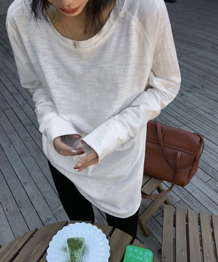 ホワイトのロングスリーブTシャツを着て、抹茶ケーキが乗った皿と、グリーンのスマホケースが置かれたクローズアップ。