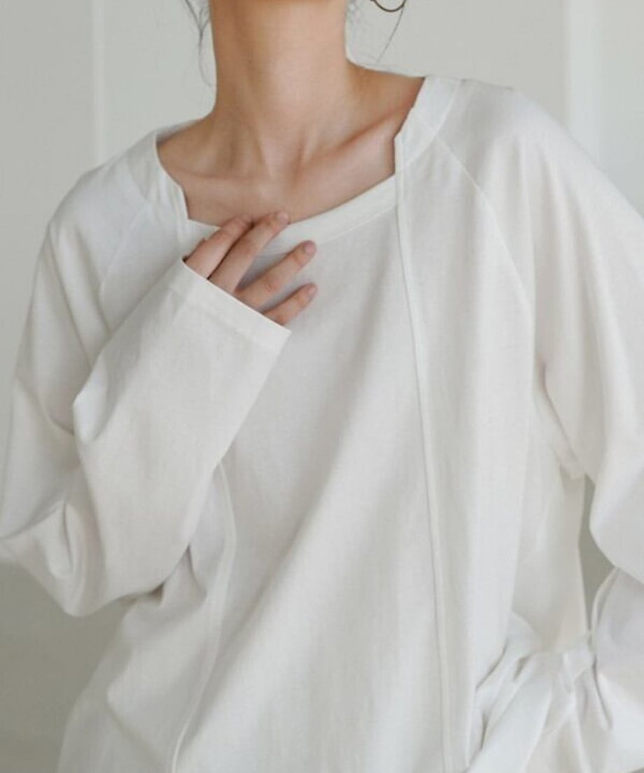 ホワイトのロングスリーブTシャツを着用した女性のバストアップ。片手を胸元に添えており、首元のスクエア風のデザインと、滑らかな生地の質感が強調されている。