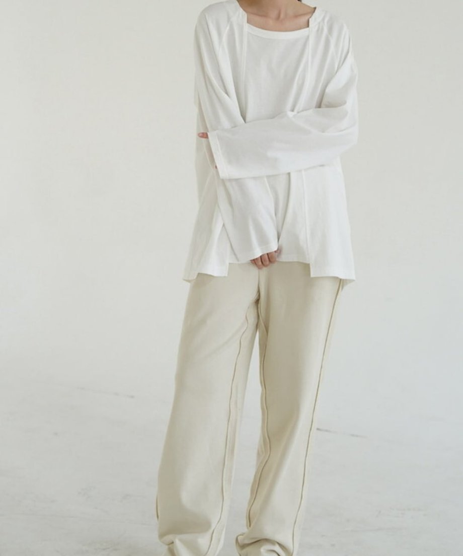 ロングスリーブTシャツを着用した女性の全身ショット。首元のデザインと、手を交差させたポーズで立っている。