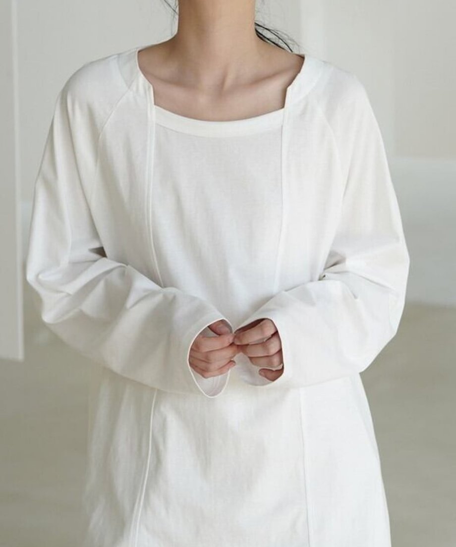 ホワイトのロングスリーブTシャツを着用した女性のバストアップ。首元はラウンドネックの上部にスクエア風の切込みがあり、前身頃中央に縦の切り替えディテールがある。
