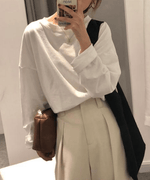 白のオーバーサイズ長袖Tシャツを着用し、スマートフォンを持ってポーズをとる女性。ベージュ系のタック入りワイドパンツ、黒い斜めがけバッグ、ブラウンのミニバッグを合わせている。