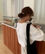 白のオーバーサイズ長袖Tシャツを着た女性が、室内のカウンターのある所に立っている後ろ姿。