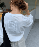 白のオーバーサイズ長袖Tシャツの後ろ姿のアップ。背中の上部に「Self-Esteem Check-Up」から始まる縦長のテキストプリントがはっきりと確認できる。